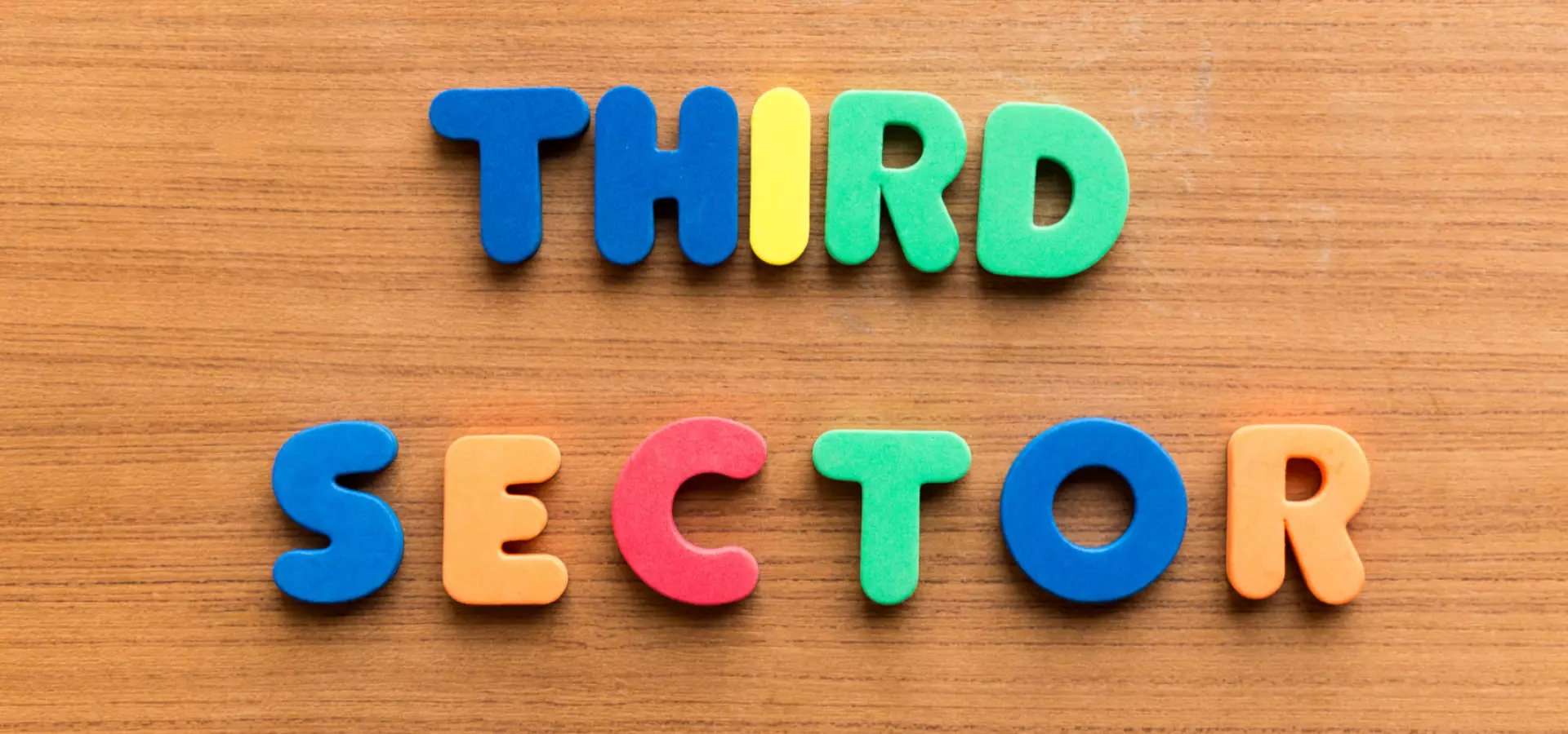 Words 'third sector' written in colourful plastic letters on a wooden background.