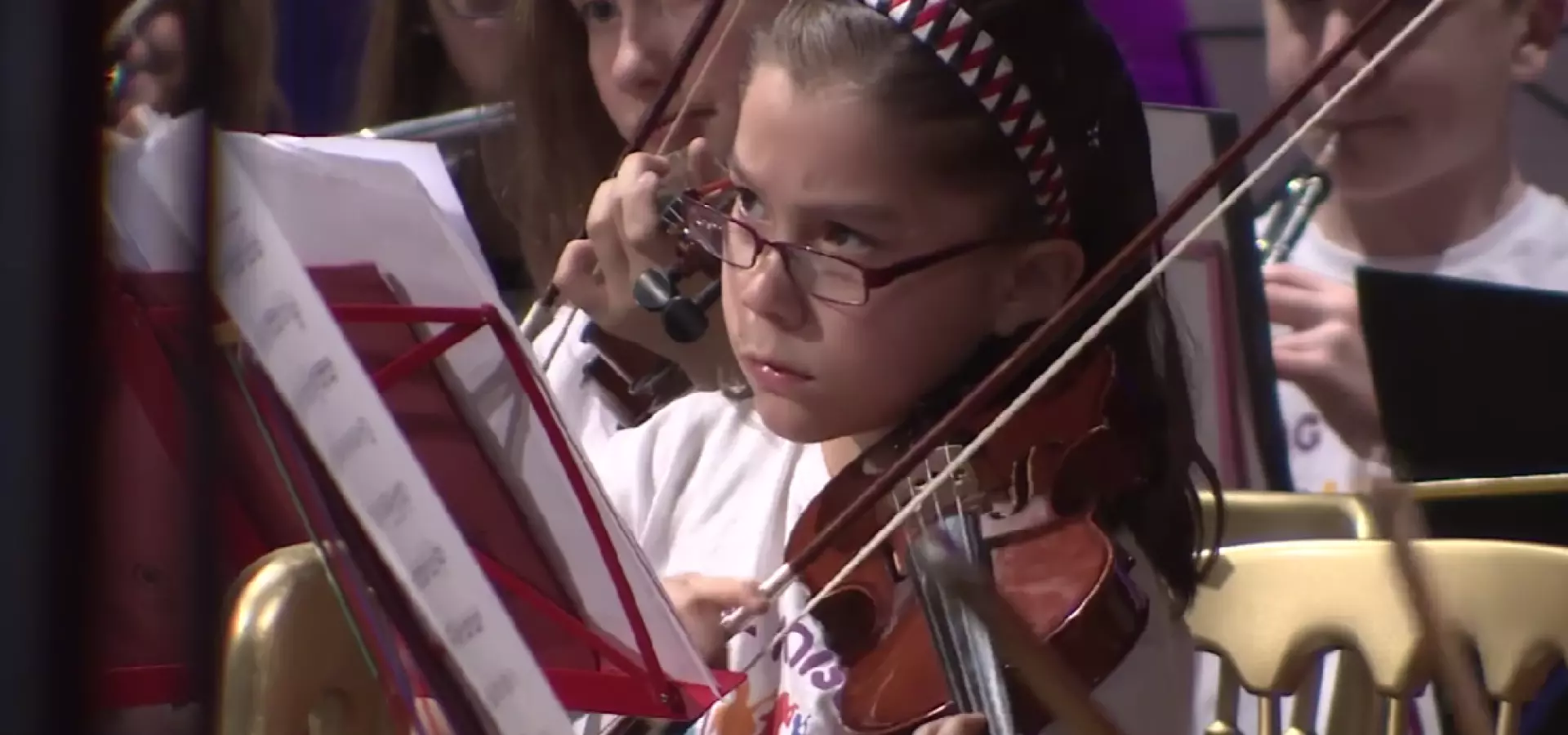 Young girl playing the fiddle, with other young musicians in the background.
