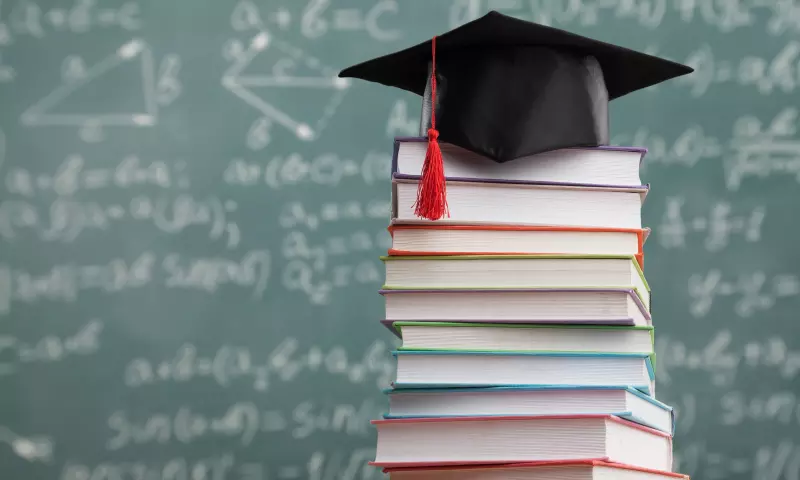 Pile of books with a graduate cap on top and a blackboard in the background.
