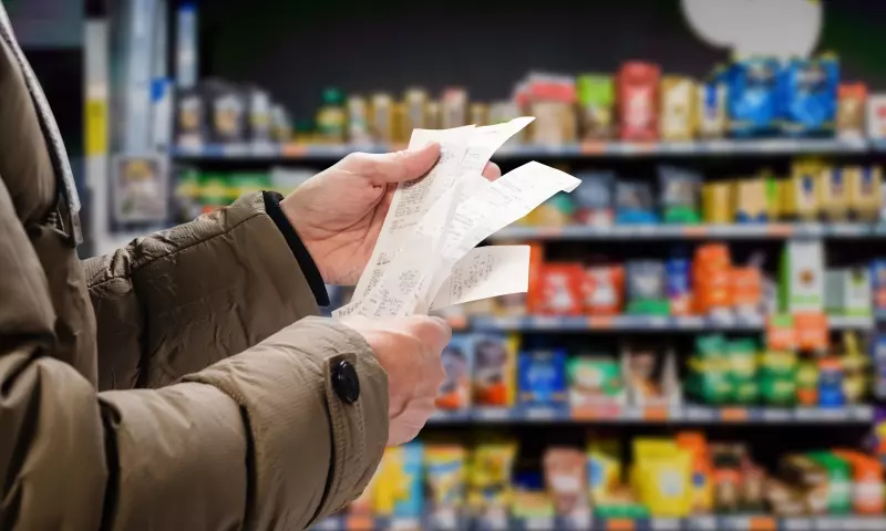 A person looking at their grocery receipt, with shop aisles in the background.