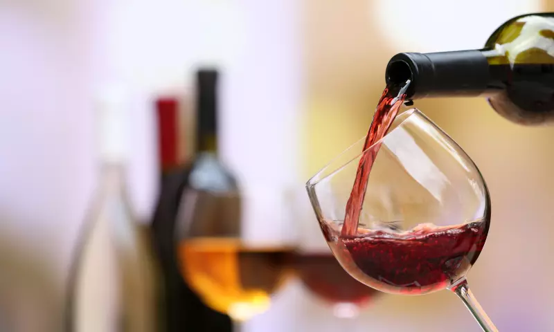 Wine being poured from a bottle into a glass. There are a couple of bottles and glasses, blurred in the background.