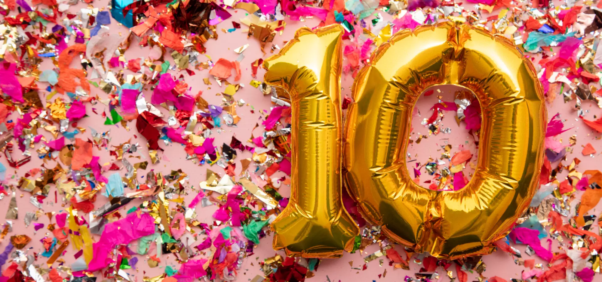 Golden balloons in the shape of '10' with colourful confetti on a pink background.