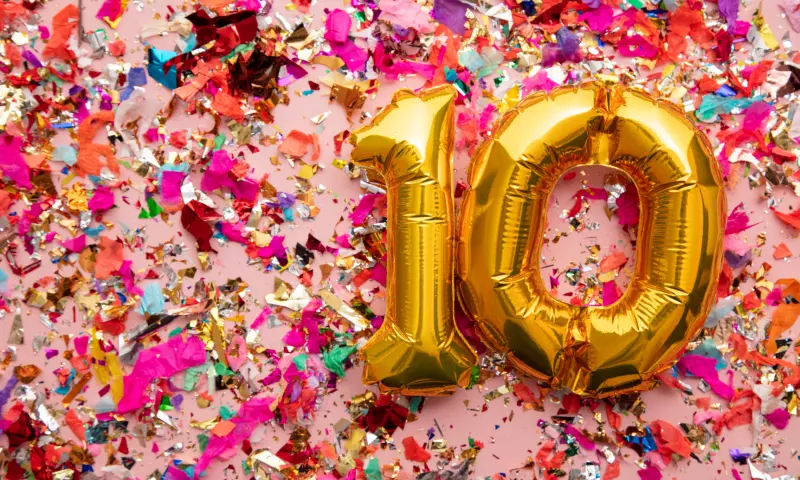 Golden balloons in the shape of '10' with colourful confetti on a pink background.