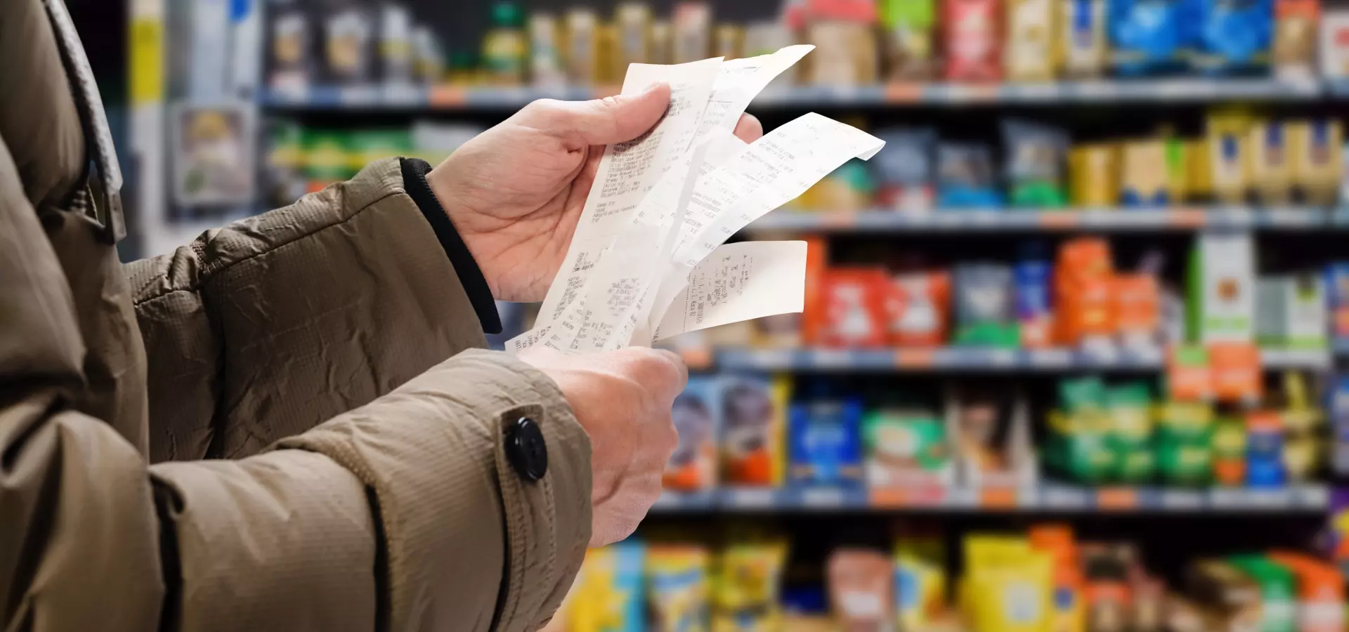 A person looking at their grocery receipt, with shop aisles in the background.