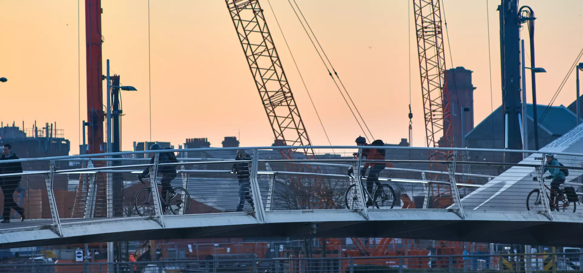 Cyclists and pedestrians crossing one of the pedestrian bridges in Glagsow, with cranes in the background.
