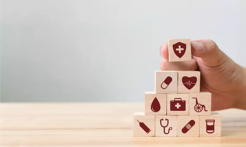Wooden cubes stacked in a pyramid with health symbols such as a heartrate, a syringe, a wheelchair etc. on each cube. 