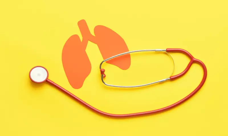 An orange paper cut out of lungs with a stethoscope on top, and yellow background.
