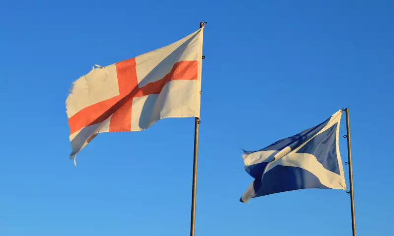 Flags of England and Scotland flying on a bright blue sky.