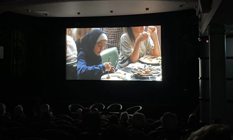 Cinema screen showing a young girl wearing a hijab, eating some food.