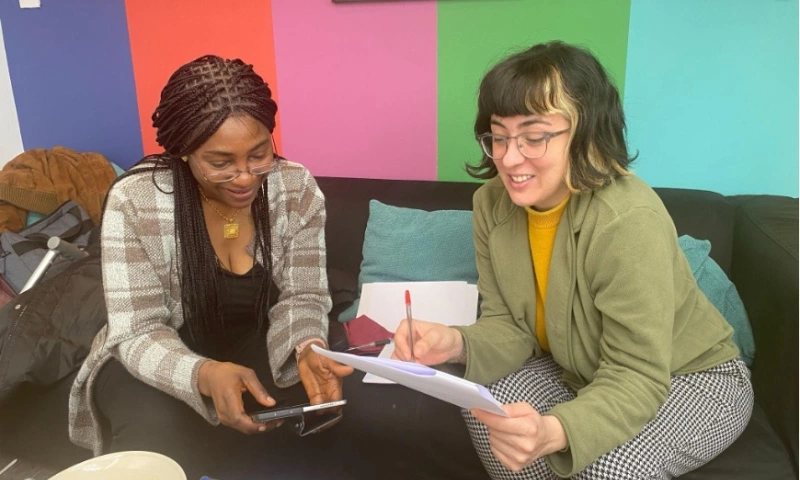 Two women sitting on a couch, talking about their research.